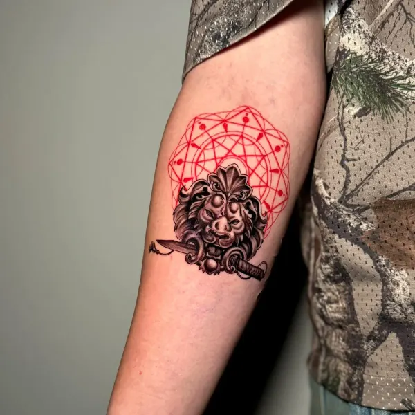 Black and grey lion with sword and red geometric halo, forearm tattoo by Cameron at Shade Studio Peterborough