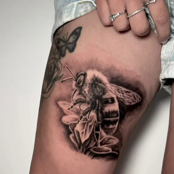 Photorealistic bee on flowers, black and grey thigh tattoo by Cameron at Shade Studio Peterborough
