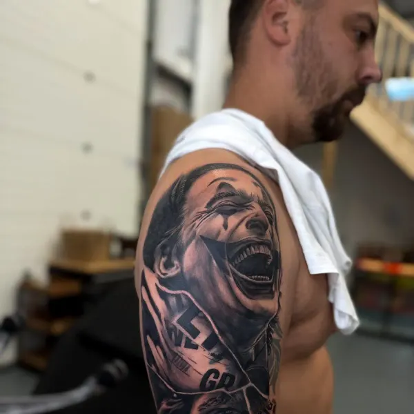 Black and grey Joker portrait with torn newspaper collage, upper arm sleeve by Kai at Shade Studio Peterborough