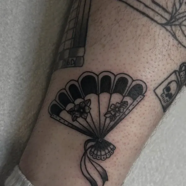 Blackwork Japanese folding fan with cherry blossom and ribbon, lower leg tattoo by Madi at Shade Studio Peterborough