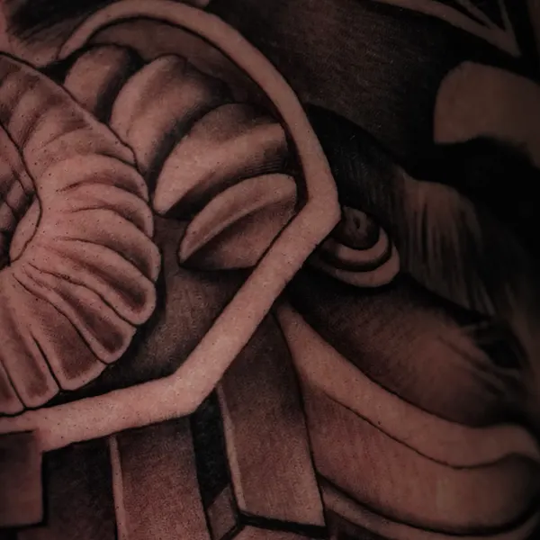 heavily shaded aztec stone carving pattern flowing across arm and hand