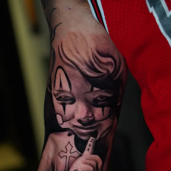 chicano clown-faced child portrait with a cross and date, forearm piece