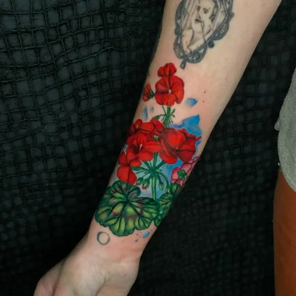 bright red geranium flowers tattooed down the wrist and forearm