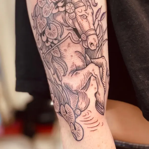 Horse among water lilies in medieval woodcut style linework, upper arm tattoo by Hannah at Shade Studio Peterborough