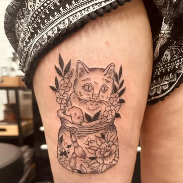 Cat sitting in a decorated flower jar, illustrative linework thigh tattoo by Hannah at Shade Studio Peterborough
