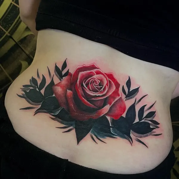 bold red rose with dark leaves tattooed across the shoulder blade